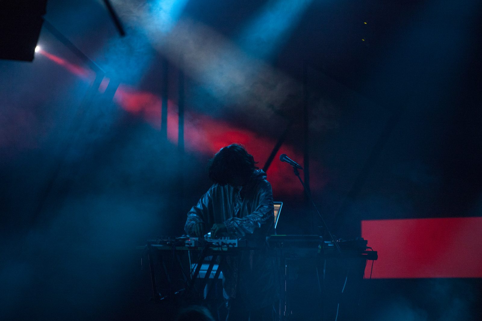 Kelly Lee Owens performing at electronic music equipment under blue and red stage lights.